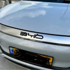 Close-up of a silver BYD car hood featuring a bold, black 3D logo emblem.