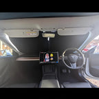 Black fabric car sunshade installed on the windshield of a white car interior.