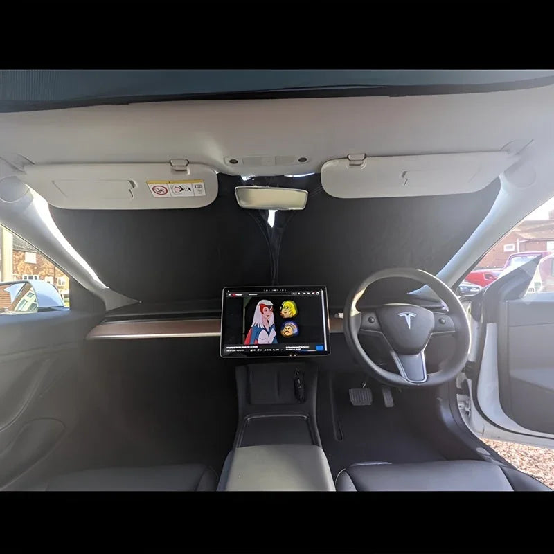Black fabric car sunshade installed on the windshield of a white car interior.
