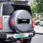 Silver metallic hard-shell spare tire cover with a sleek black decorative emblem on a grey SUV.