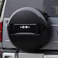 Glossy black hard-shell spare tire cover with a sleek silver emblem on a grey SUV.