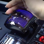 Hand adjusting a sleek, black glossy gear shifter with blue LED light accents and illuminated gear indicators.