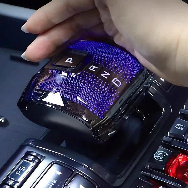 Hand adjusting a sleek, black glossy gear shifter with blue LED light accents and illuminated gear indicators.
