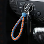 Braided blue and orange leather car key fob strap hanging from a vehicle ignition switch.