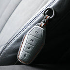 Black leather car key cover with orange stitching attached to a zipper