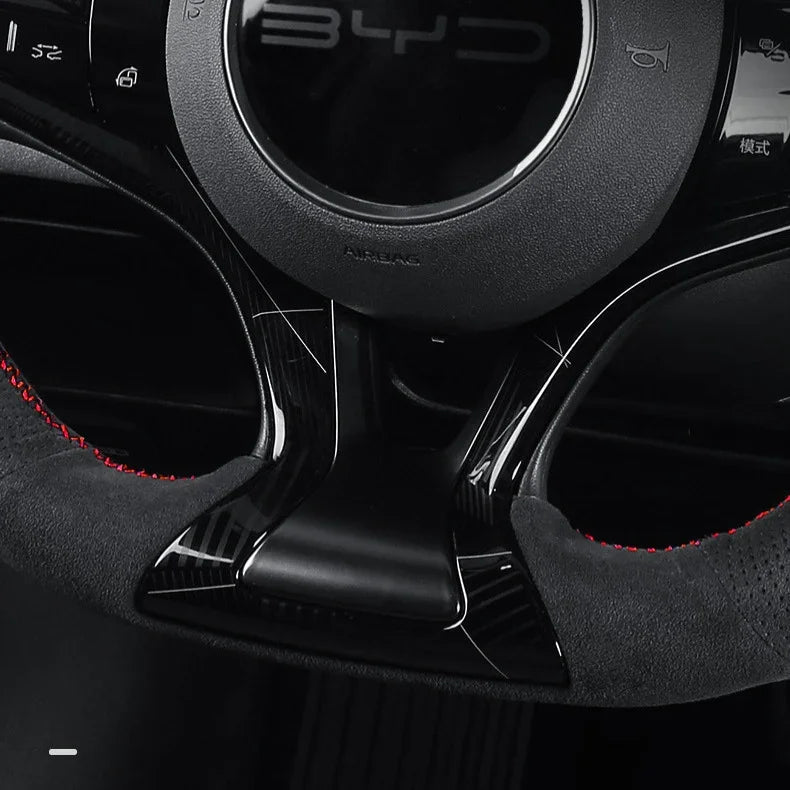 Black carbon fiber steering wheel trim with red stitching and premium suede texture.