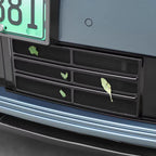 Close-up of a black mesh rear bumper grille with leaves caught in the slots.