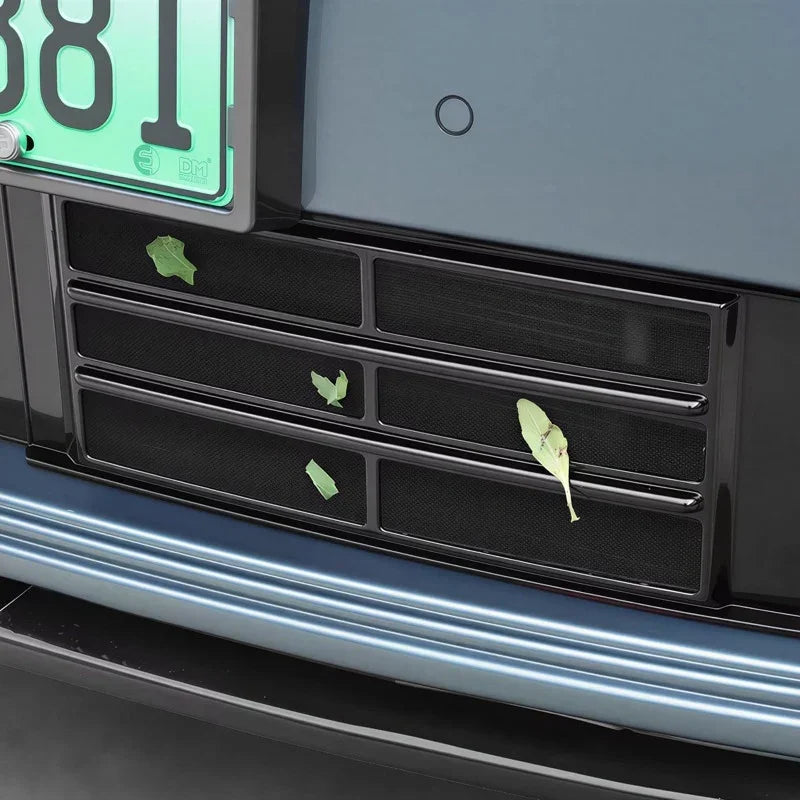 Close-up of a black mesh rear bumper grille with leaves caught in the slots.