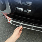 Black protective bumper guard strip with red accents being installed on a car bumper.