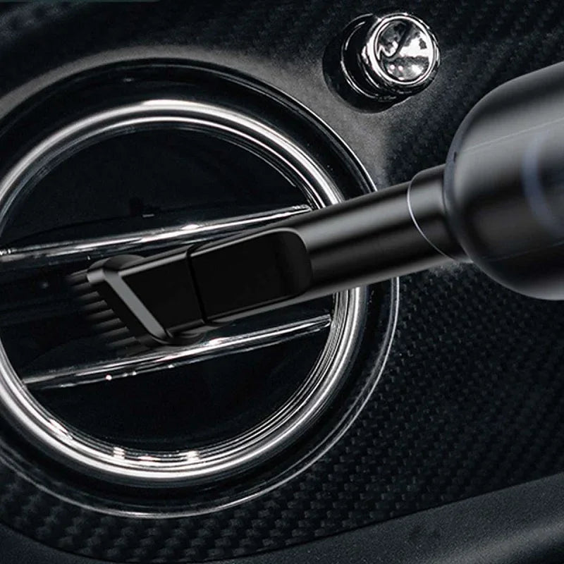 Black soft-bristle detailing brush cleaning a chrome-rimmed car air vent on carbon fiber trim.