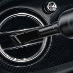 Black soft-bristle detailing brush cleaning a chrome-rimmed car air vent on carbon fiber trim.