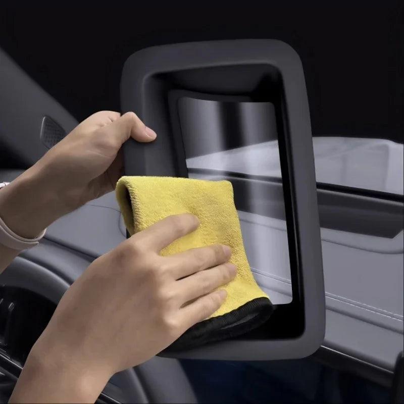 Hands cleaning a black matte car dashboard screen with a soft yellow microfiber cloth.