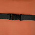 Close-up of a black nylon strap with a plastic buckle on a brown leather surface.