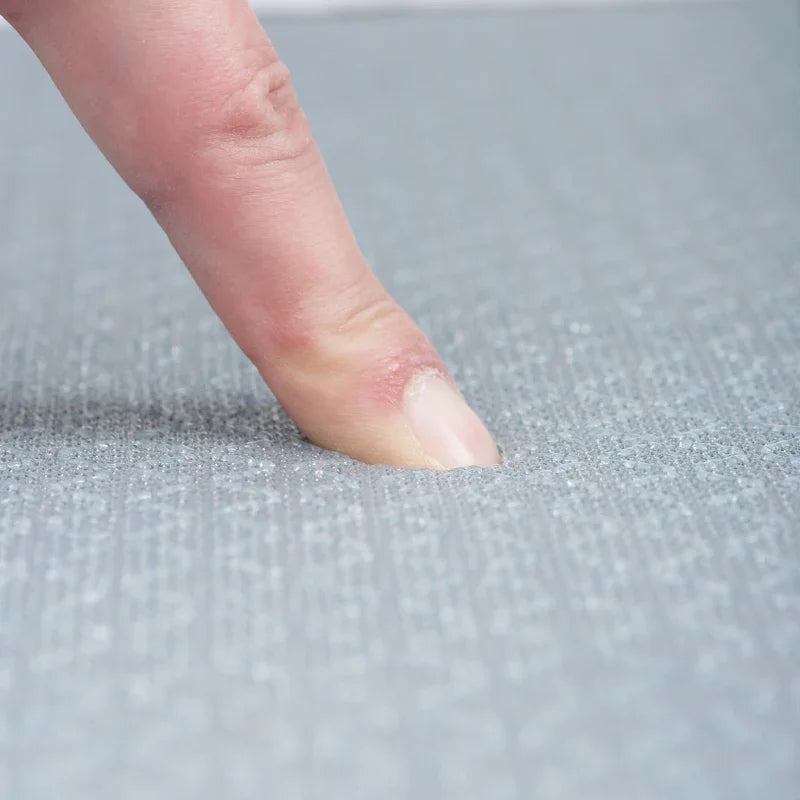 Close-up of a finger touching a textured, light grey waterproof car mat material.