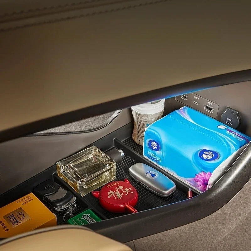 Organized car center console storage featuring a blue tissue box and various small accessories.