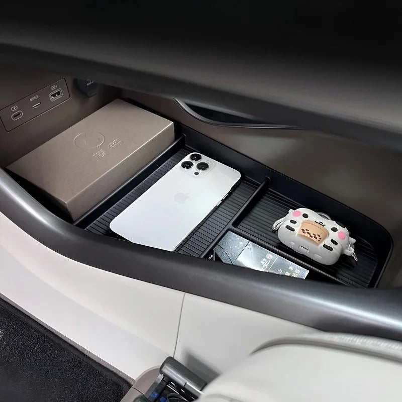Black textured organizer tray in a car console holding a white smartphone and accessories.