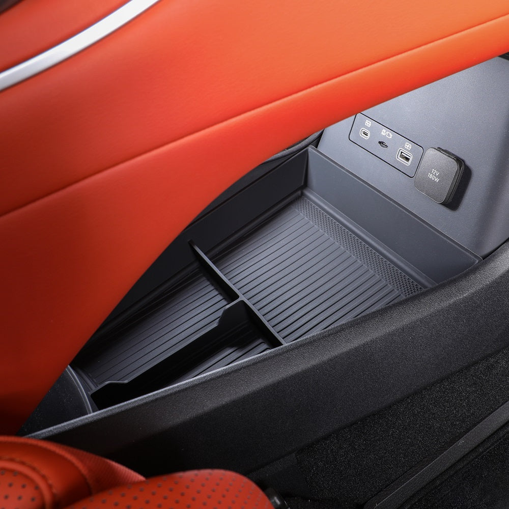 Black textured plastic car organizer tray installed in an orange leather interior with USB ports.