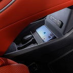 Close-up of a black plastic car storage console with a smartphone and key fob near red leather seats.