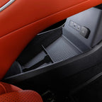 Black plastic center console storage tray with USB ports and power outlet, orange leather interior.