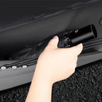 A hand placing a black compact foldable umbrella into a sleek car door storage pocket.