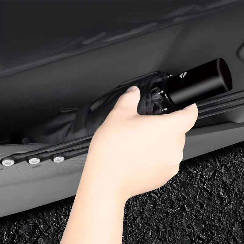A hand placing a black compact foldable umbrella into a sleek car door storage pocket.