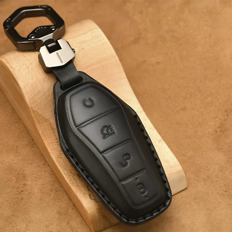 Premium black leather car key cover with a metal carabiner on a light wood surface.
