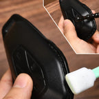 Black textured leather car key fob cover being cleaned with a white sponge.