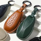 Premium leather car key fob covers in brown, dark green, and beige with precise stitching.