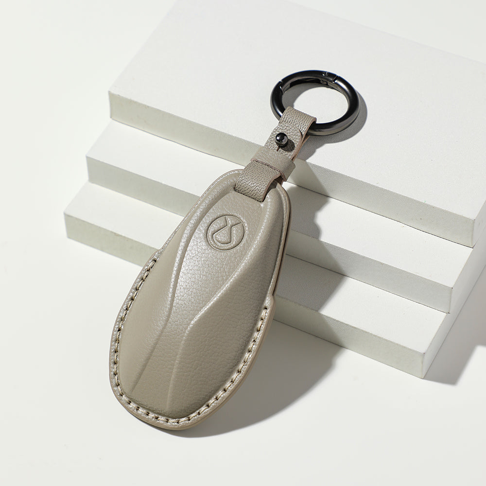 Premium beige leather car key fob cover with embossed logo and white stitching.