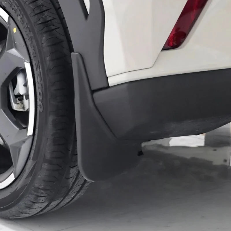 Close-up of a matte black durable plastic mud guard installed on a white vehicle wheel arch.