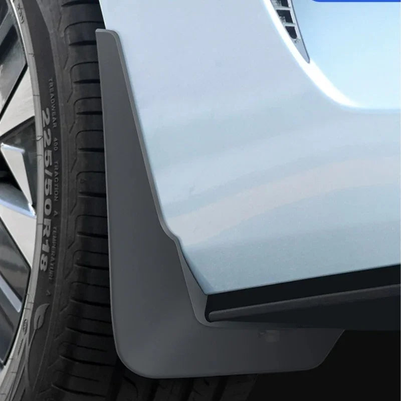 Black matte TPU mud flap installed behind the front wheel of a light blue car for protection.
