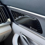 Black Dirac premium audio speaker grille with metallic silver trim on a dark leather car interior.