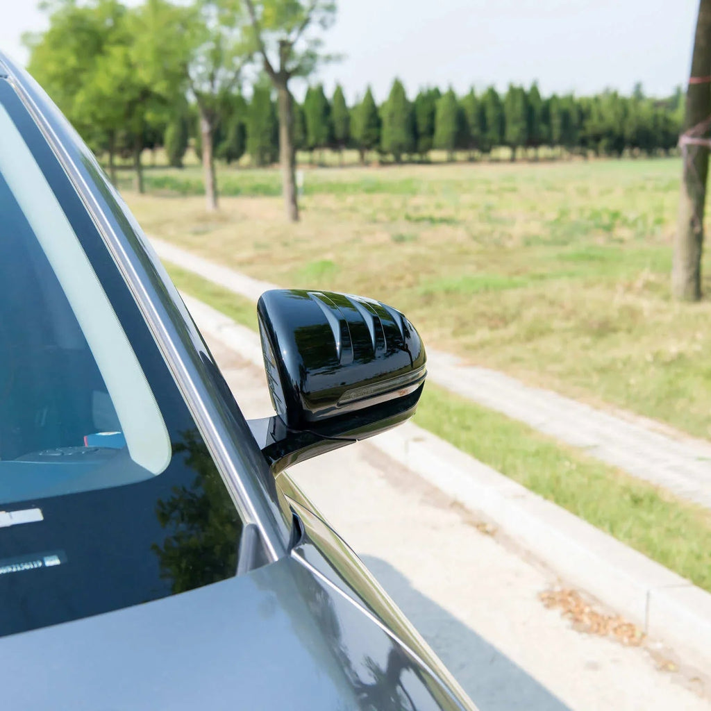 Glossy black side mirror housing with integrated LED turn signal on a grey vehicle.