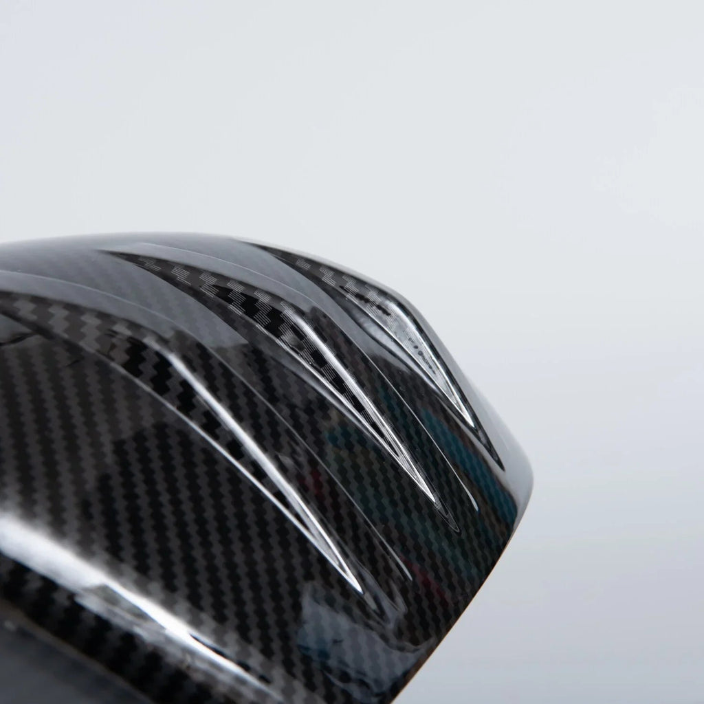 Close-up of a glossy black carbon fiber automotive accessory with a textured weave pattern.
