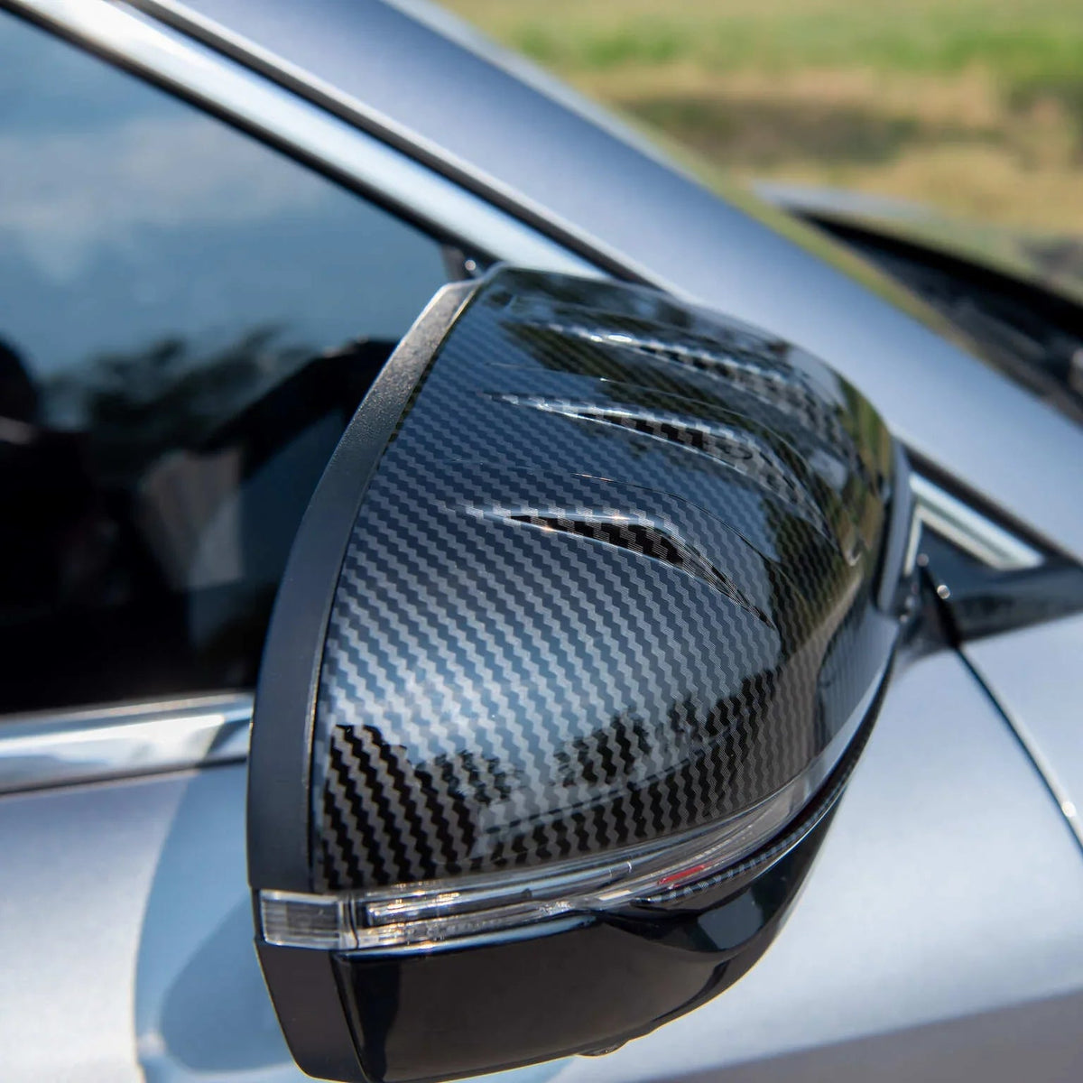 Close-up of a car side mirror cover featuring a sleek black carbon fiber texture finish.