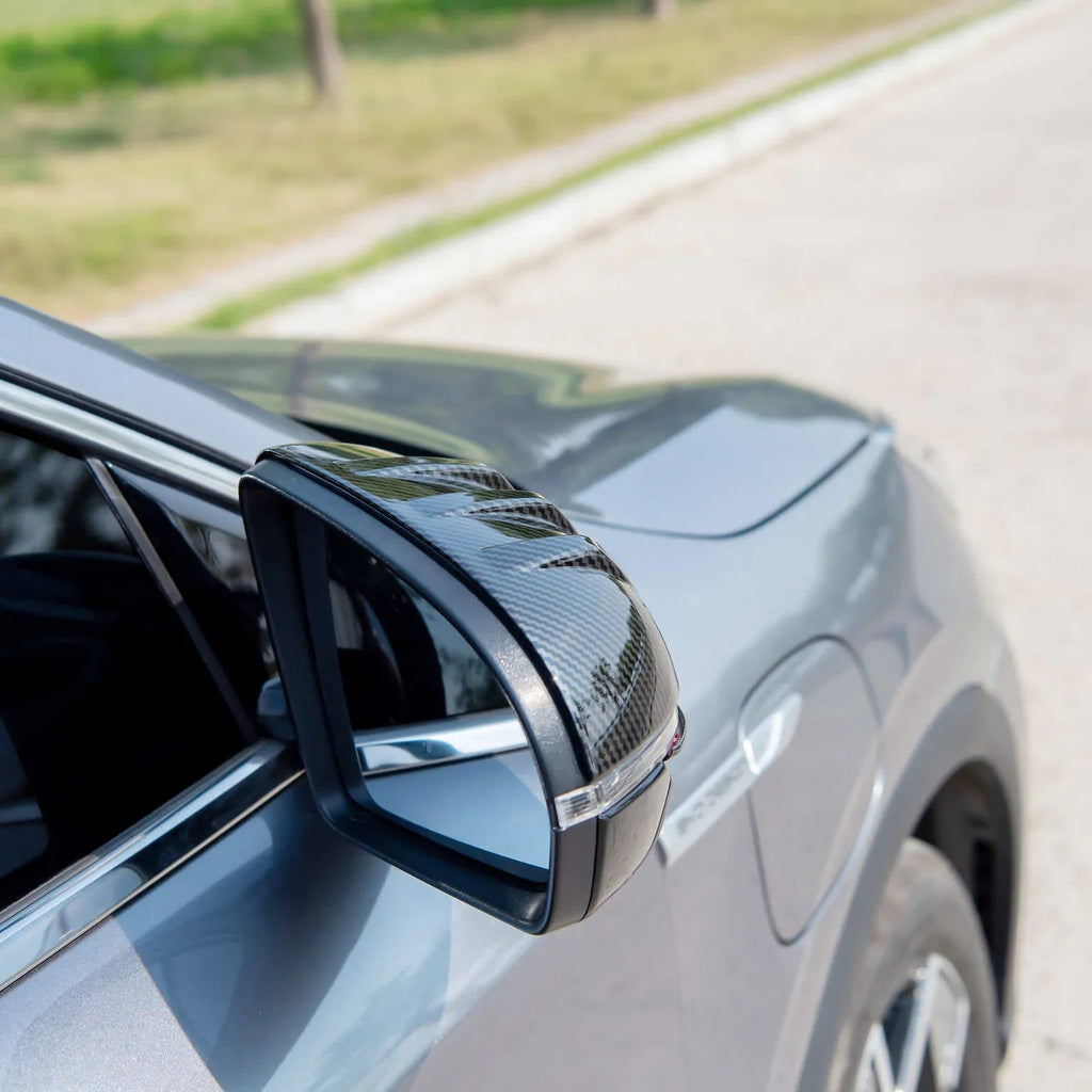 Carbon fiber side mirror cover with a sleek black weave pattern on a grey car.