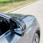 Carbon fiber side mirror cover with a sleek black weave pattern on a grey car.