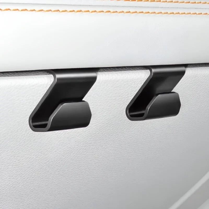 Two matte black durable plastic seat back hooks mounted on a white leather car interior.