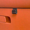 Black matte plastic door handle hook mounted on premium orange leather car interior trim.