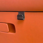 Black matte plastic door handle hook mounted on premium orange leather car interior trim.