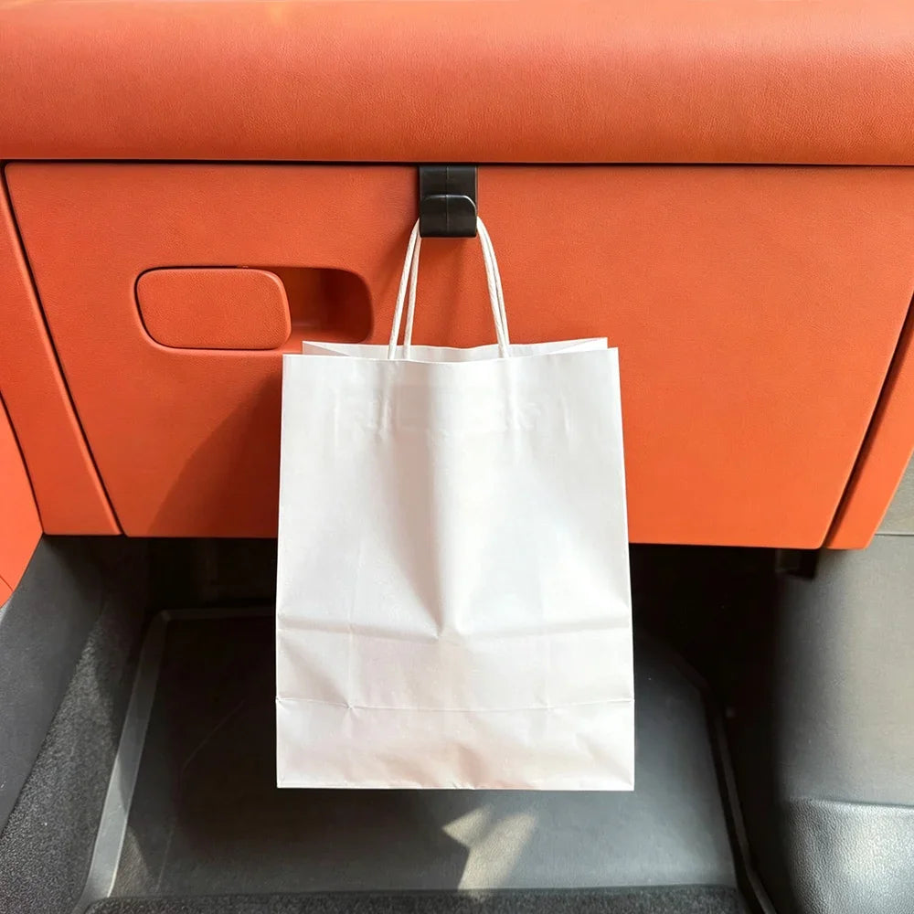 White paper shopping bag hanging from a black hook on orange leather car seat back.