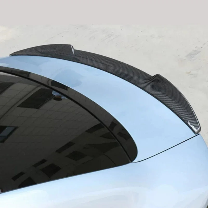 Black carbon fiber rear spoiler installed on a light blue car trunk for aerodynamic styling.