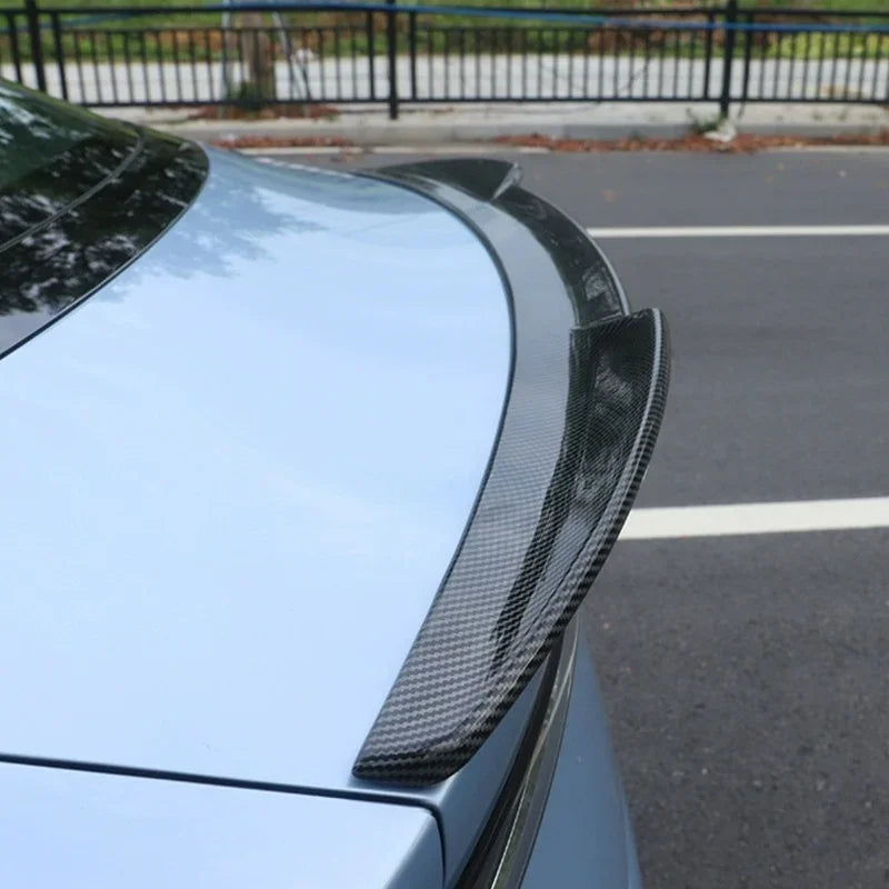 Carbon fiber rear spoiler installed on a light blue car for enhanced aerodynamics.