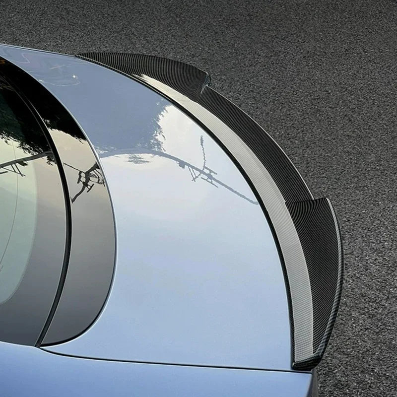 Black carbon fiber rear spoiler installed on a light blue car for enhanced aerodynamics.