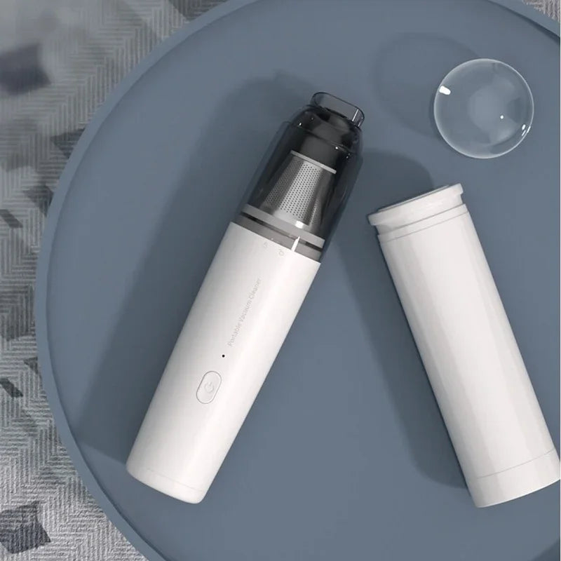 Portable handheld vacuum cleaner in white with a transparent dust collector on a blue tray.