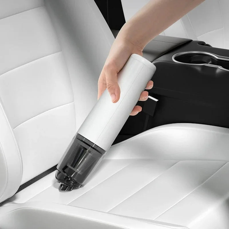 Hand using a white handheld cordless car vacuum cleaner on white leather car seats.