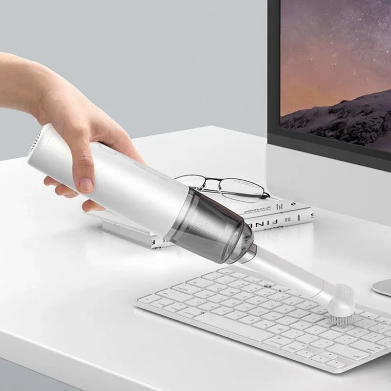 Hand using a sleek white portable handheld vacuum cleaner to clean a white computer keyboard.