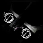 Two glowing white DENZA logo car door welcome lights projecting on a dark surface.