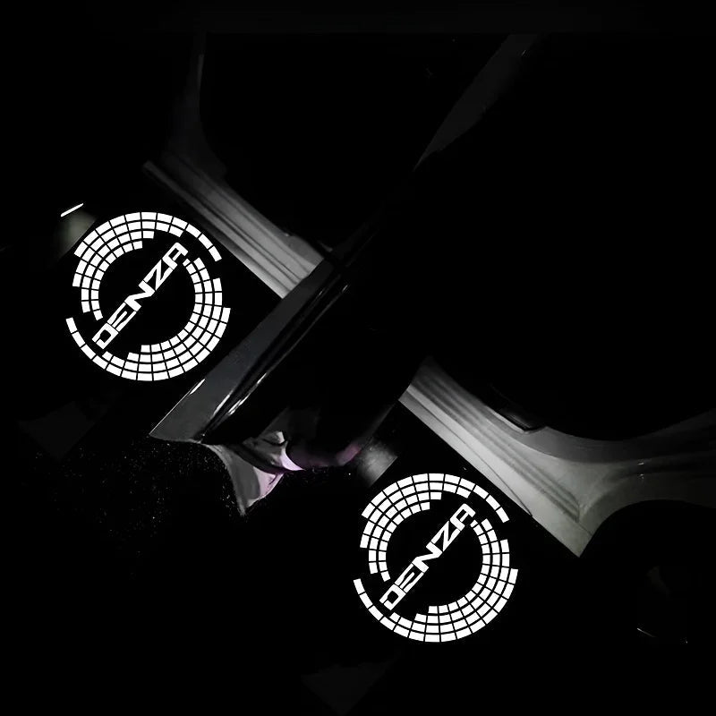 Two glowing white DENZA logo car door welcome lights projecting on a dark surface.