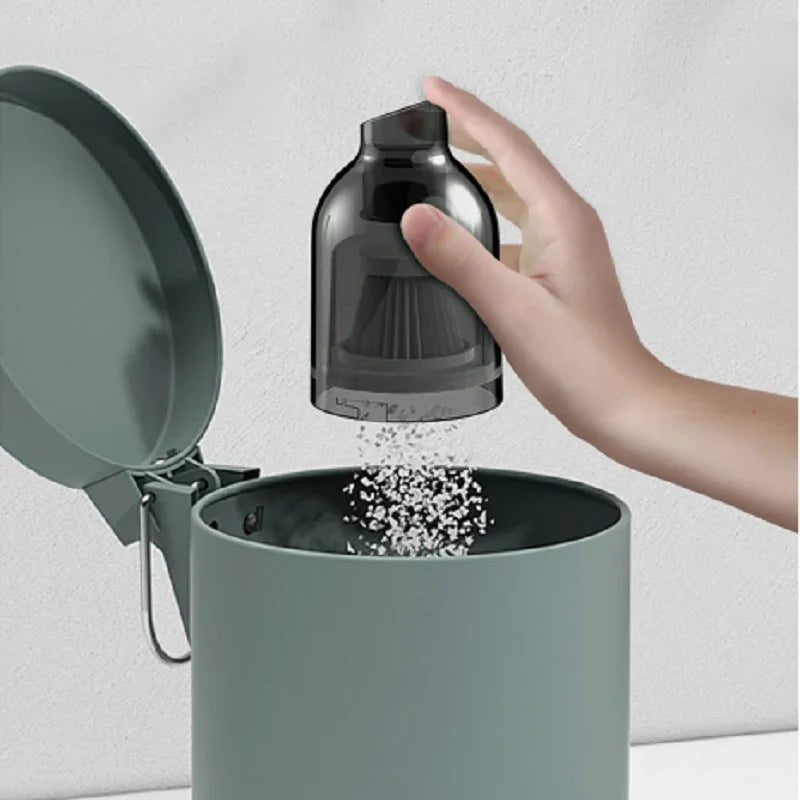 Hand pouring white granules from a transparent black plastic dispenser into a matte grey bin.